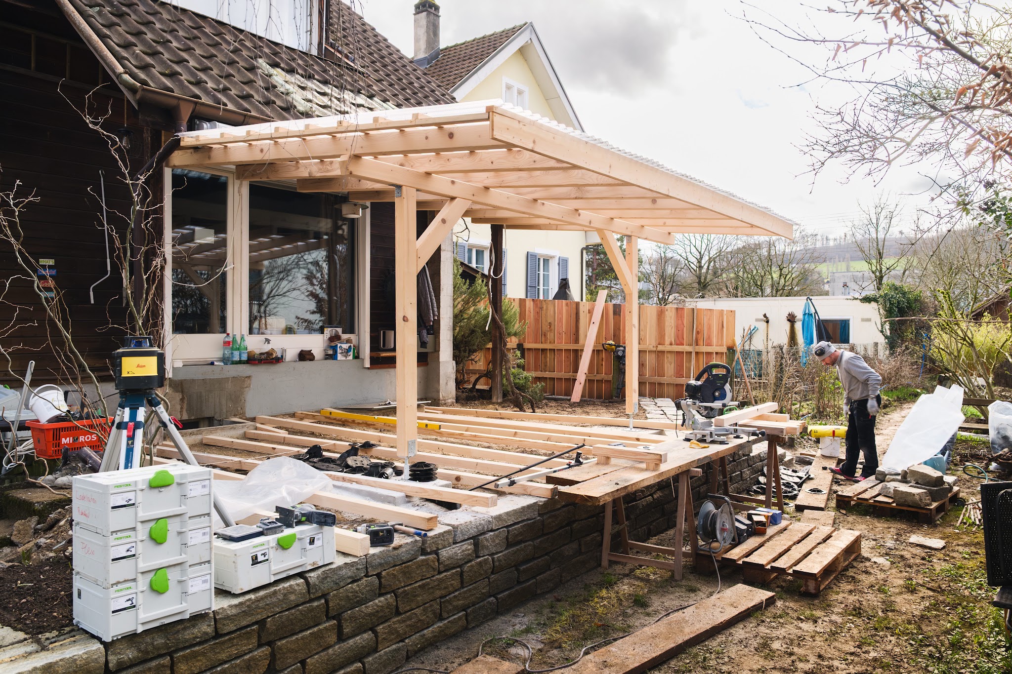 Holzpergola und Terrasse im Bau mit Werkzeugkoffern und Laser