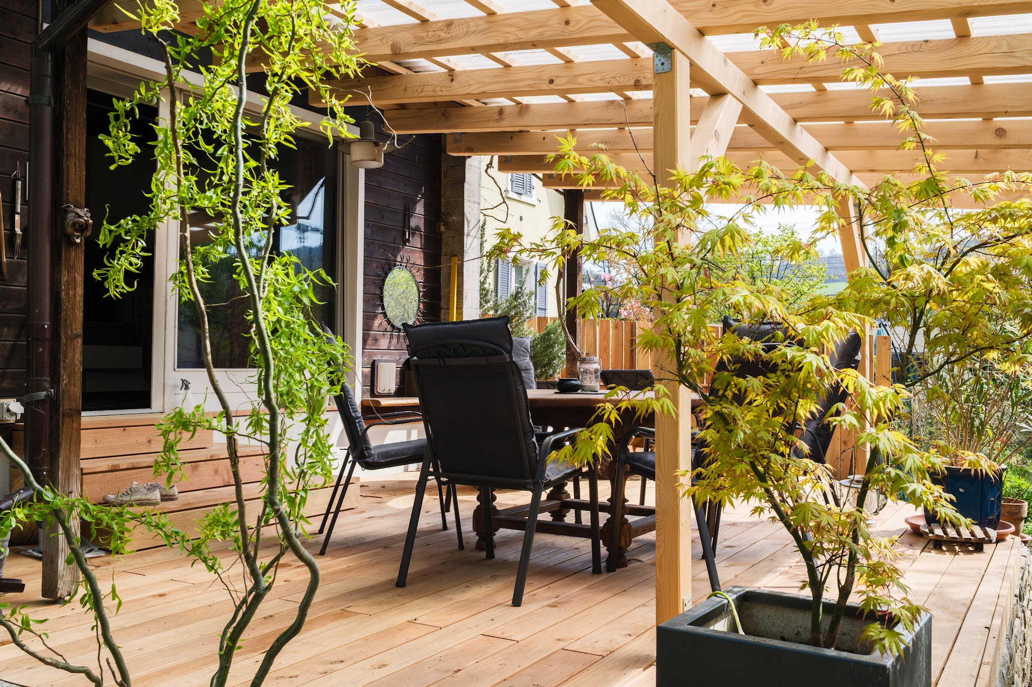 Fertige Holzterrasse unter einer Pergola mit Pflanzen und Gartenmöbeln